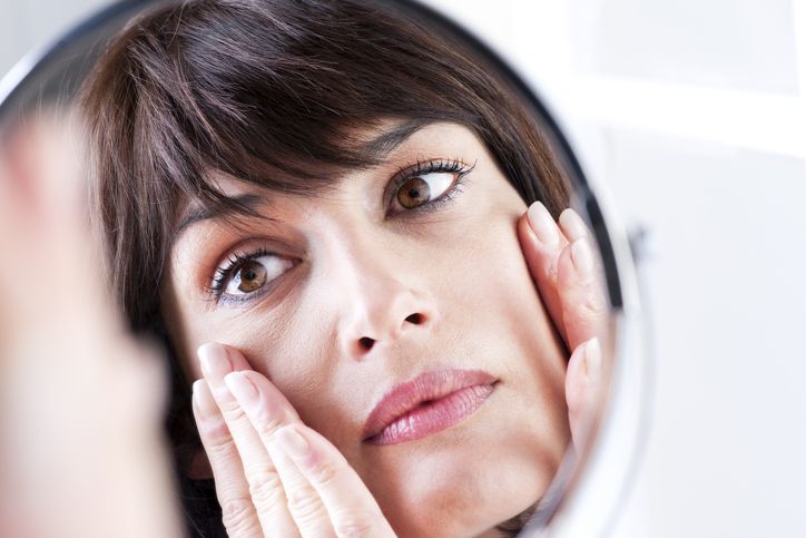 5 stvari koje odaju vaše godine i kako usporiti starenje kože; žena koja posmatra svoj odraz u ogledalu