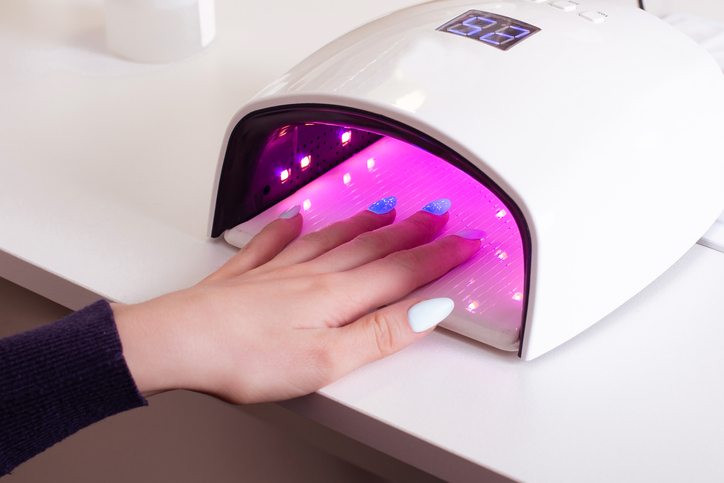 Da li je gel lak opasan; devojka drži ruku u UV lampi za učvršćivanje gel laka na noktima