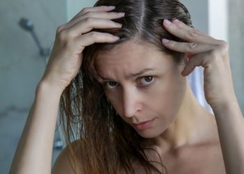 Navike koje ubrzavaju pojavu sede kose; mlada devojka zabrinuto gleda sede vlasi u svojoj kosi