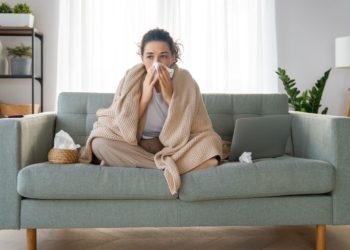 Respiratorne infekcije: Kako da se brzo opravite od gripa i prehlade; žena sedi na krevetu ogrnuta ćebetom i bori se sa simptomima gripa