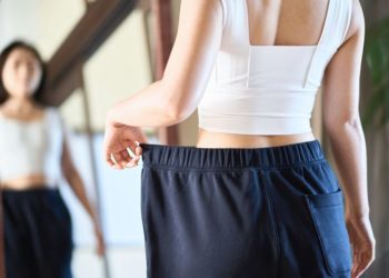 Zamke brzog mršavljenja: Da li je loše naglo izgubiti težinu; žena stoji ispred ogledala i rukom pridržava preveliku trenerku