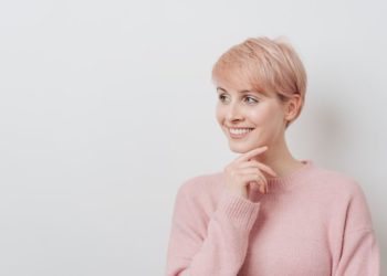 Idealne frizure za okruglo lice koje će biti u modi 2024; prelepa žena u nežno roze džemperu i kratkom rose gold kosom
