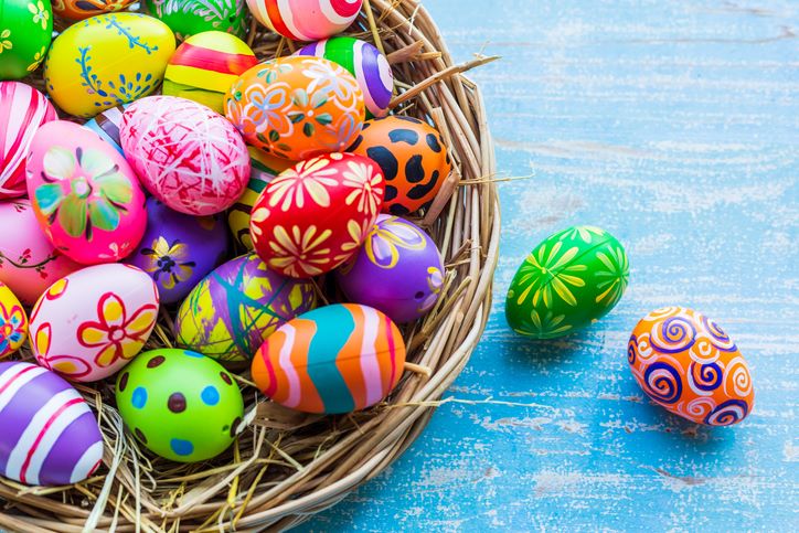 Najkreativnije ideje za farbanje uskršnjih jaja; prelepo ukrašena, šarena jaja u korpi od pruća na plavoj, drevenoj površini