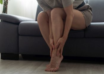 Zašto otiču noge i kako to sprečiti; žena sedi na krevetu i masira svoje noge