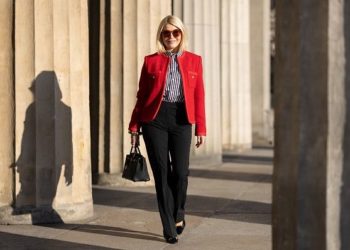 Bezvremenske dizajnerske torbe koje nikada neće izaći iz mode; Plavokosa žena u crvenom blejzeru, košulji na bruge i crnim pantalonama nosi crnu Hermes Birkin torbu