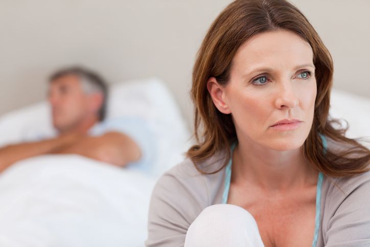5 znakova da brak narušava vaše zdravlje; nezadovoljna žena, smeđe kose sedi na ivici kreveta, okrenuta leđima muškarcu koji spava