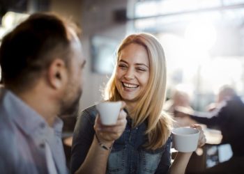 znak da ga privlačite; žena i muškarac sede u kafići, piju kafu i smeju se