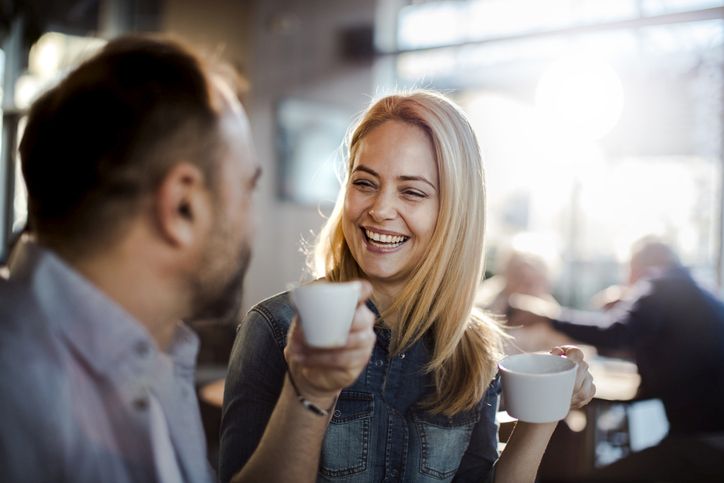 znak da ga privlačite; žena i muškarac sede u kafići, piju kafu i smeju se