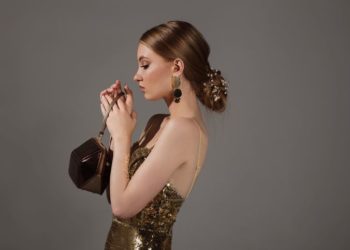 Najlepše frizure za maturu: Elegantne i raskošne; elegantna mlada devojka slikana iz profila, u svečanoj haljini, sa ukrašenom niskom punđom, drži elegantnu torbicu