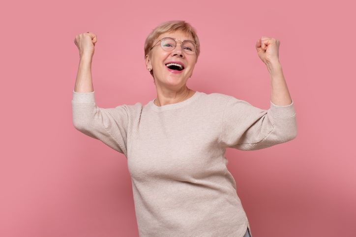 Vitamini D3 i K2 sprečavaju osteoporozu; srećna šezdesetogodišnjakinja pozira sa podignutim rukama
