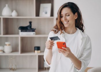 Merkur kreće direktno 25. aprila; nasmejana, dugokosa žena u beloj košulji drži u jednoj ruci telefon a u drugoj kreditnu karticu